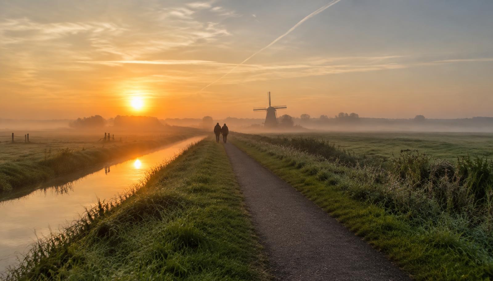 Twee wandelaars op een polderpad bij zonsopgang